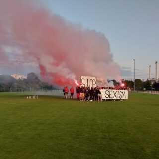 Demo auf Fussballfeld mit Stop-Sexism-Banner und roten Bengalos